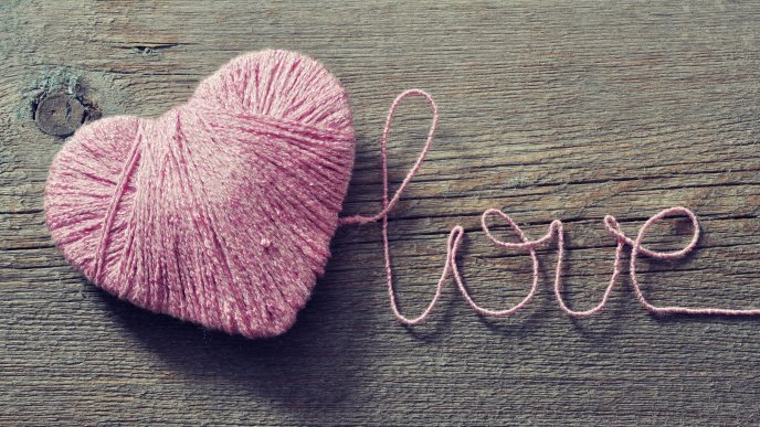 A pink heart made of wool on the wood