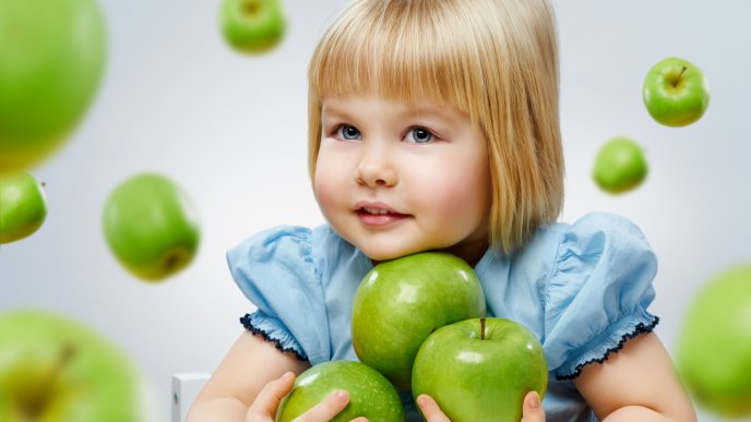 A sweet girl in blue with many green apples in her arms